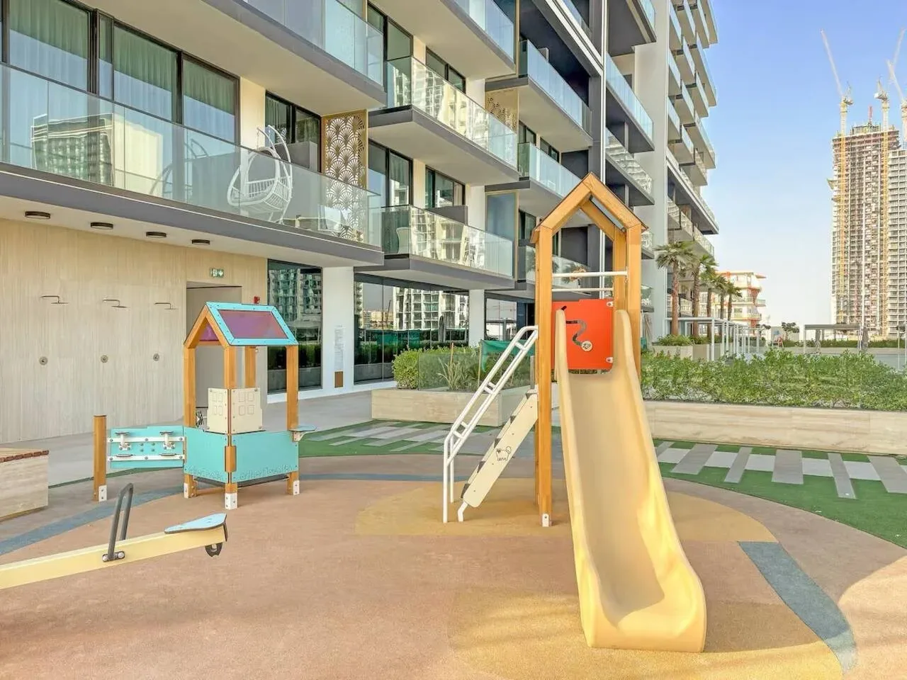 Un parque infantil al aire libre con tobogán y casita junto a un edificio de apartamentos moderno.