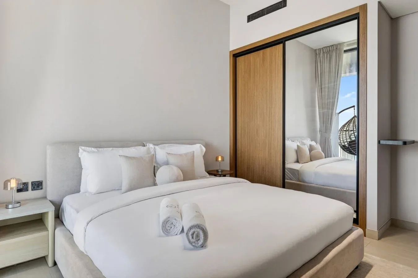 Un dormitorio luminoso con una cama bien arreglada y un armario con espejo.
