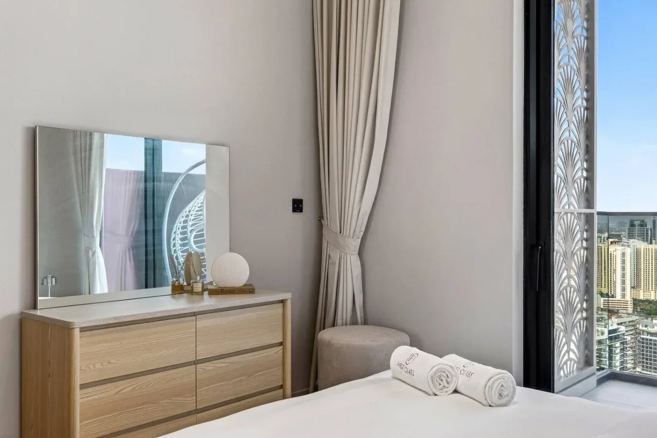 Dormitorio con cama, cómoda y una ventana grande con edificios a la vista.