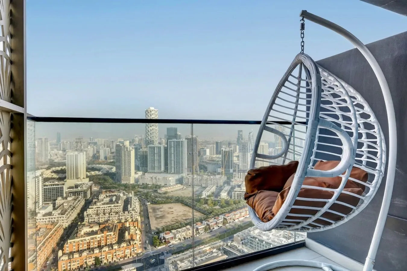 Un balcón con una silla colgante ofrece vistas de un denso horizonte urbano.