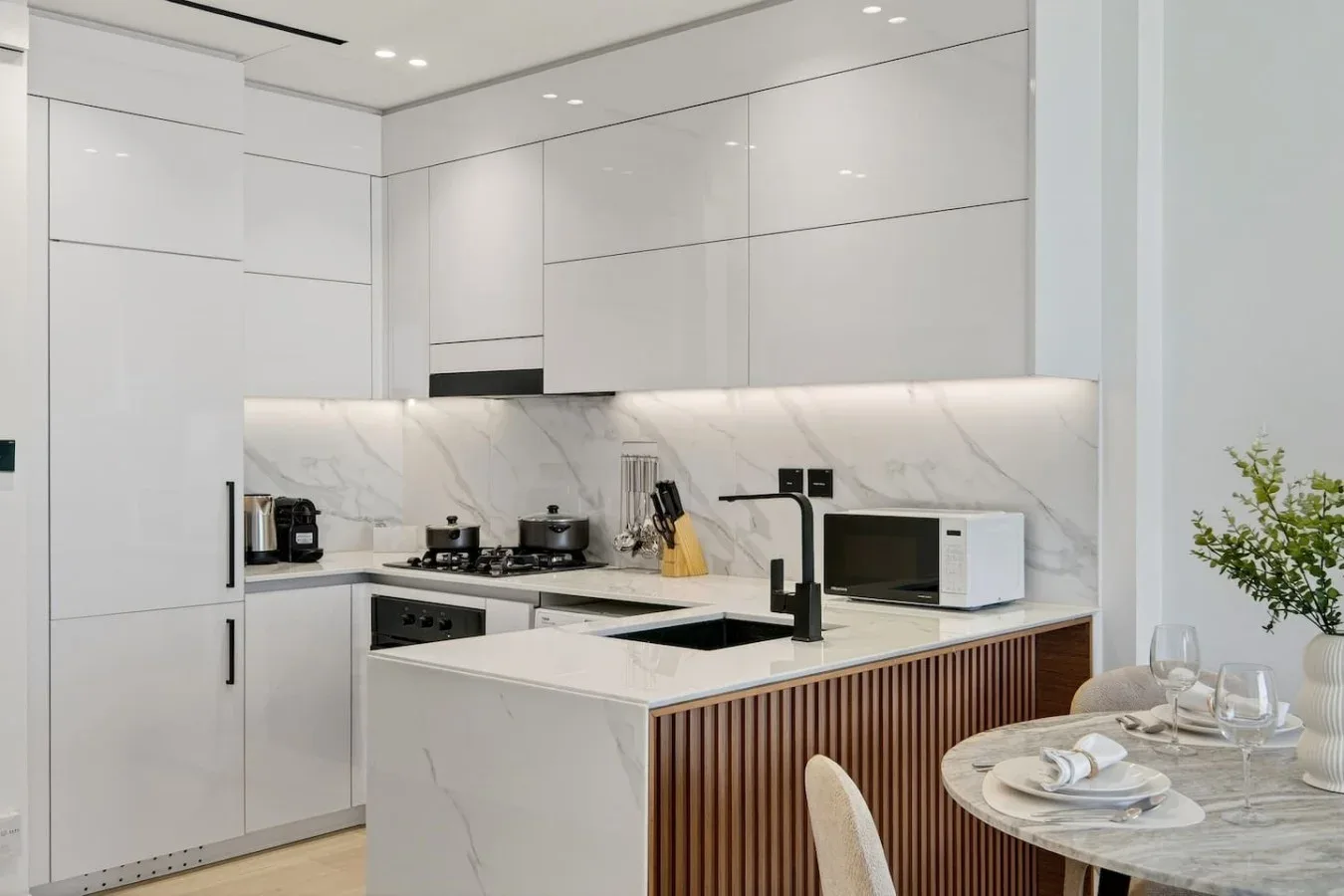Una cocina blanca moderna con una isla y una mesa de comedor al lado.