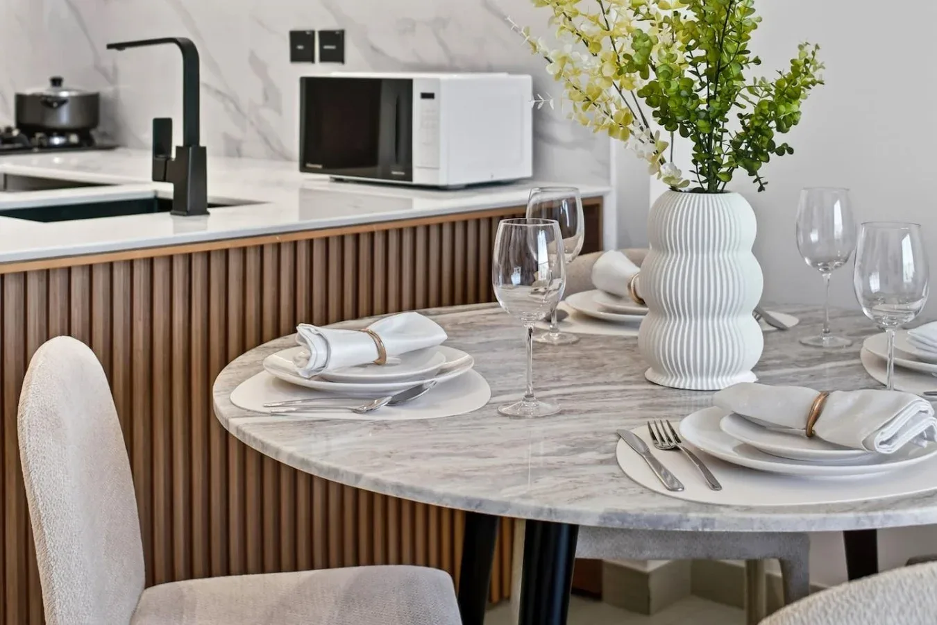 Una mesa de comedor está puesta con platos y copas junto a una encimera de cocina.