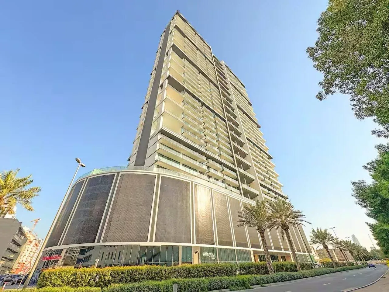 Un edificio moderno de gran altura se alza junto a una calle ajardinada bajo un cielo despejado.