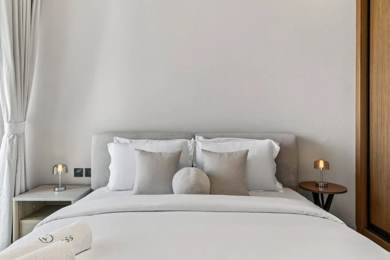 Una cama bien arreglada con ropa de cama blanca, cojines neutros y mesas de noche.