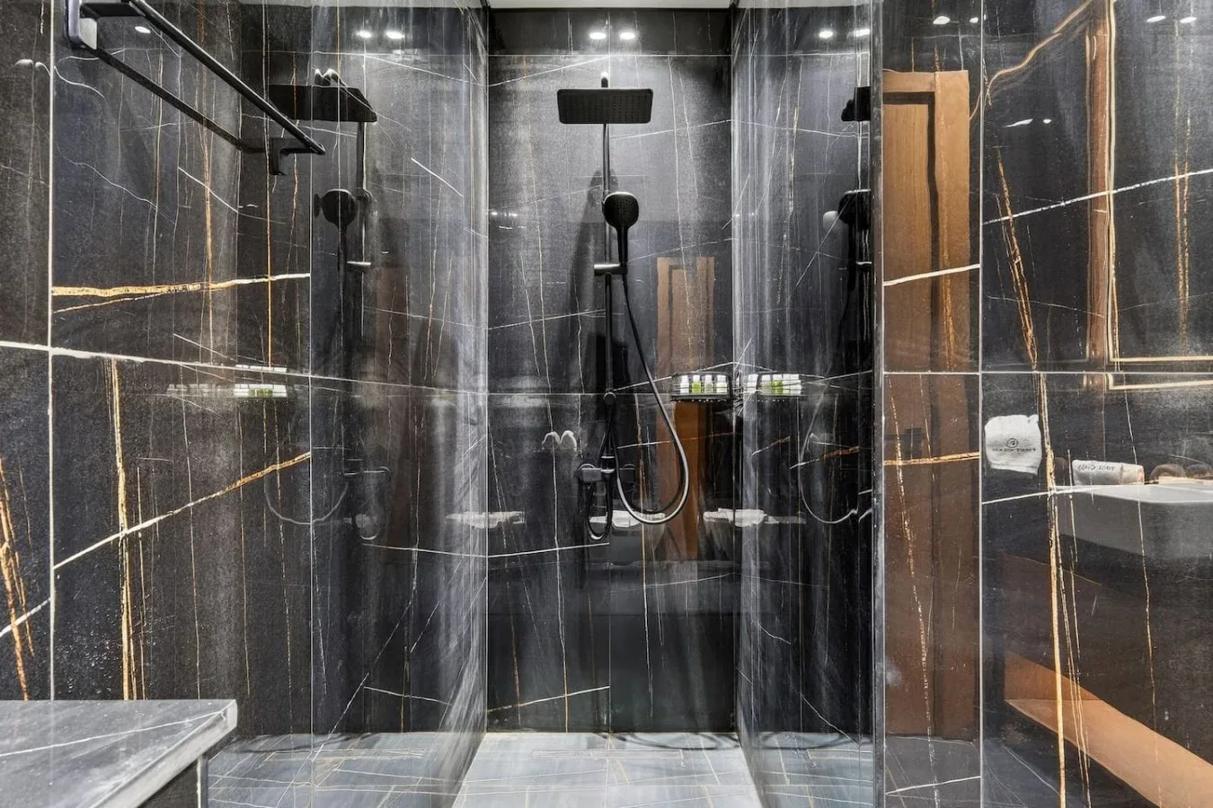 Un baño de azulejos oscuros con ducha de lluvia y paneles de vidrio.