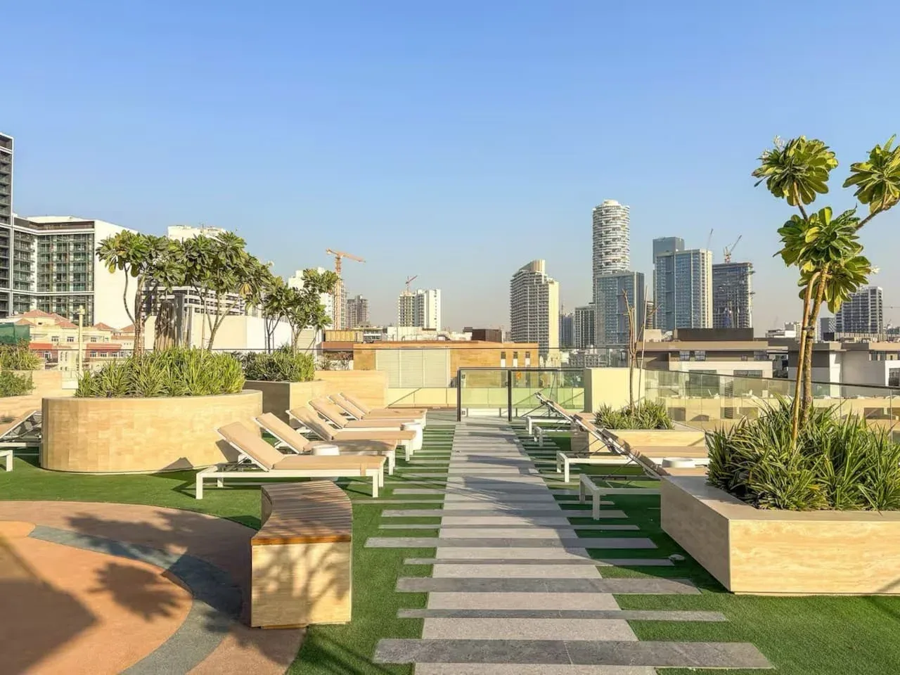 Una terraza en la azotea tiene un sendero pavimentado, asientos, jardineras y edificios de la ciudad.