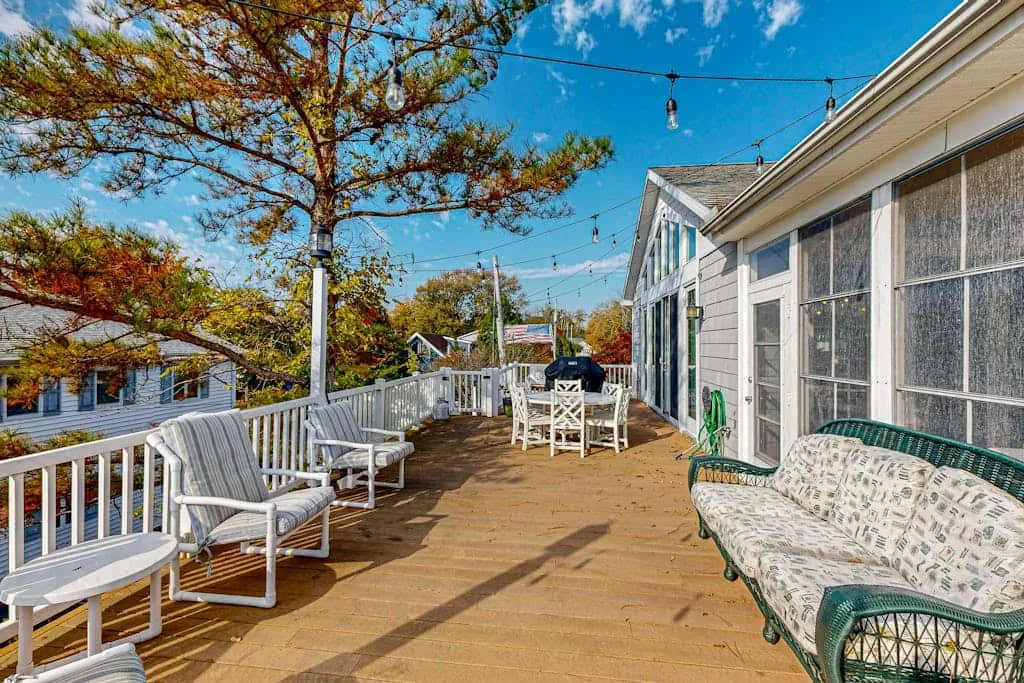 A wooden deck beside a light-colored house has outdoor seating and string lights.