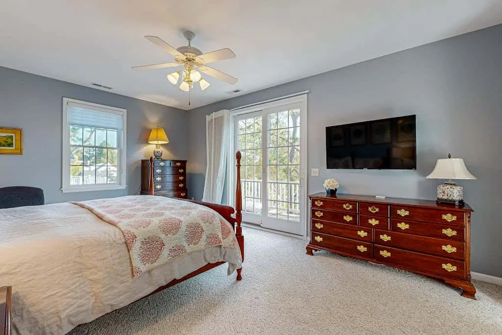 A bedroom with a bed, dresser, and glass doors opening onto a bright view.