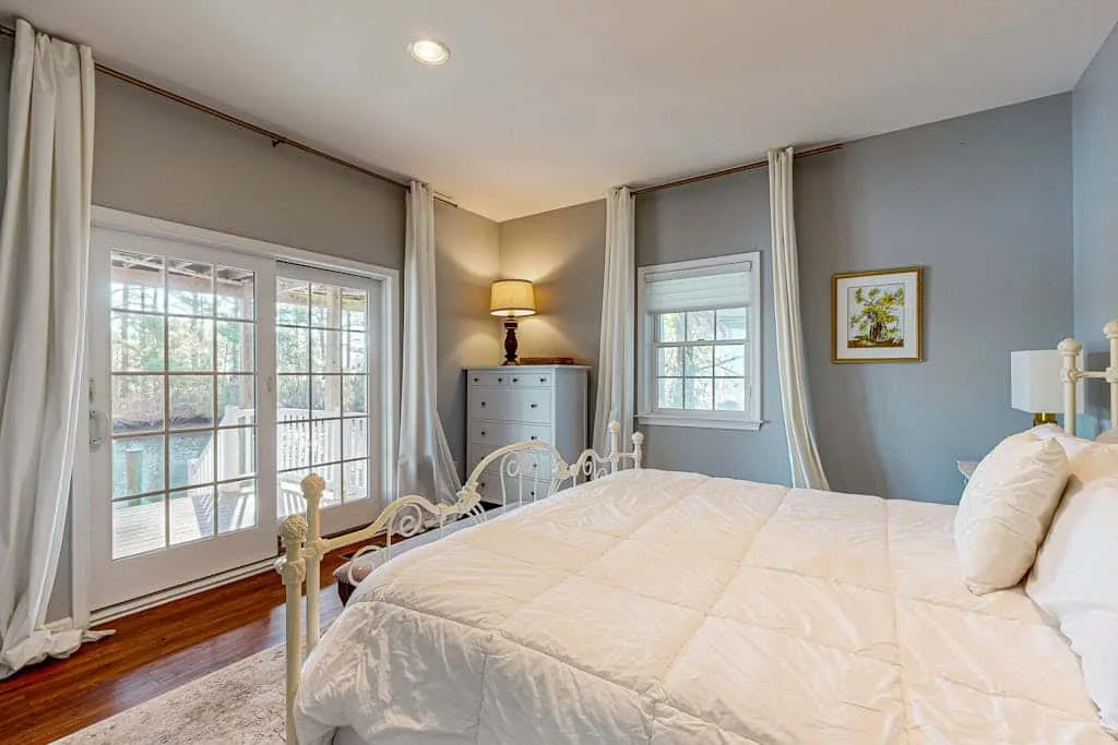 A bright bedroom with a large bed, tall windows, and light curtains.