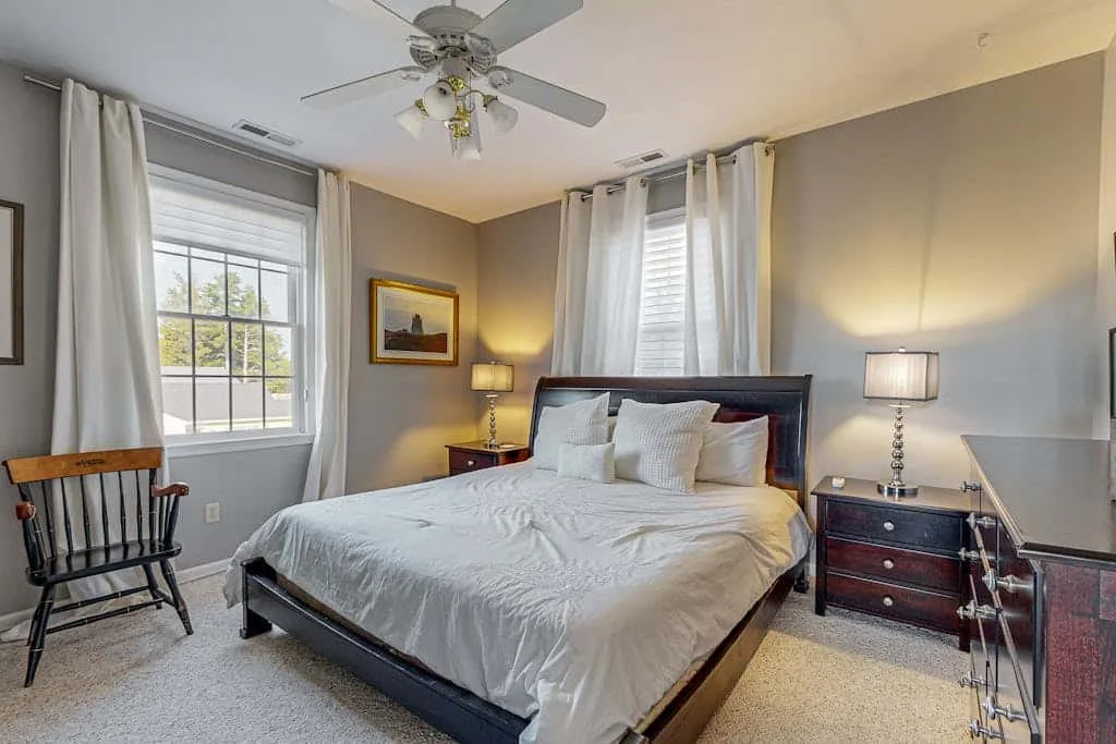 A bedroom with a large bed, bedside lamps, and windows with light curtains.