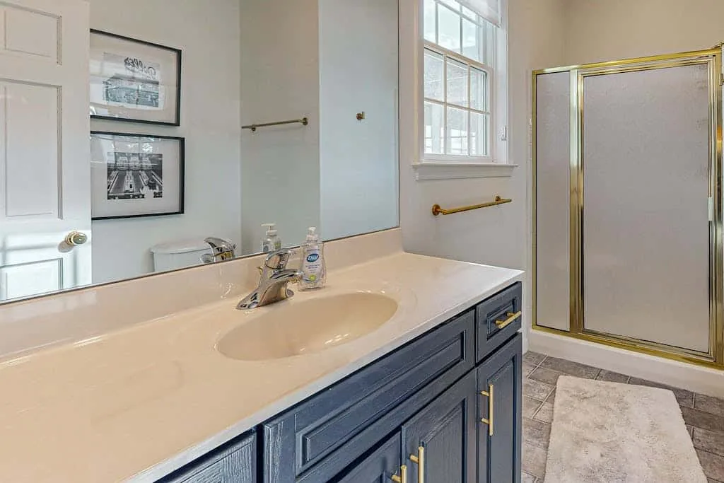 A bright bathroom vanity with a wide counter, window, and glass shower.