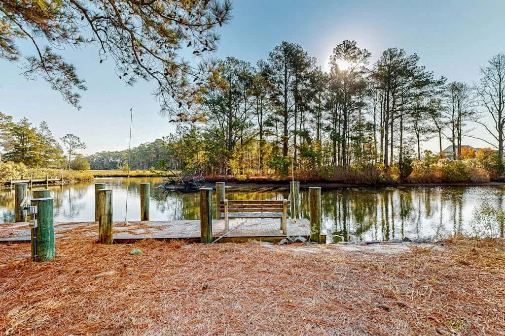 A lakeside dock sits beside calm water, with trees lining the opposite shore.