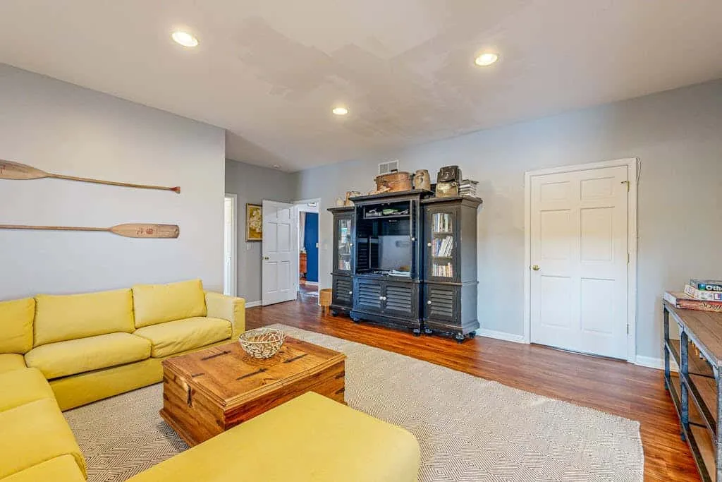 A living room with yellow seating, a wooden coffee table, and a large entertainment cabinet.