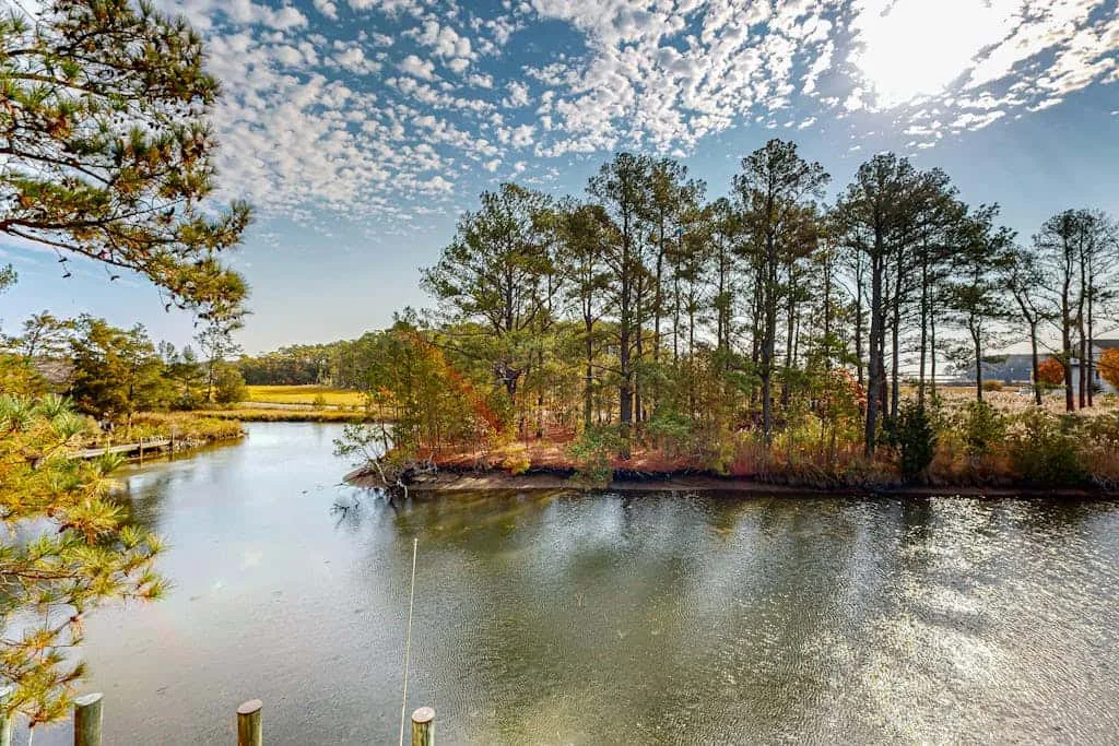 A tree-lined pond reflects the bright, partly cloudy sky.