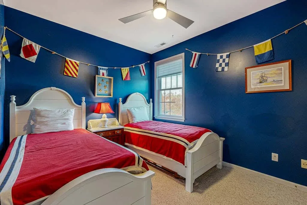 A bedroom with two beds, blue walls, and colorful flags hanging overhead.