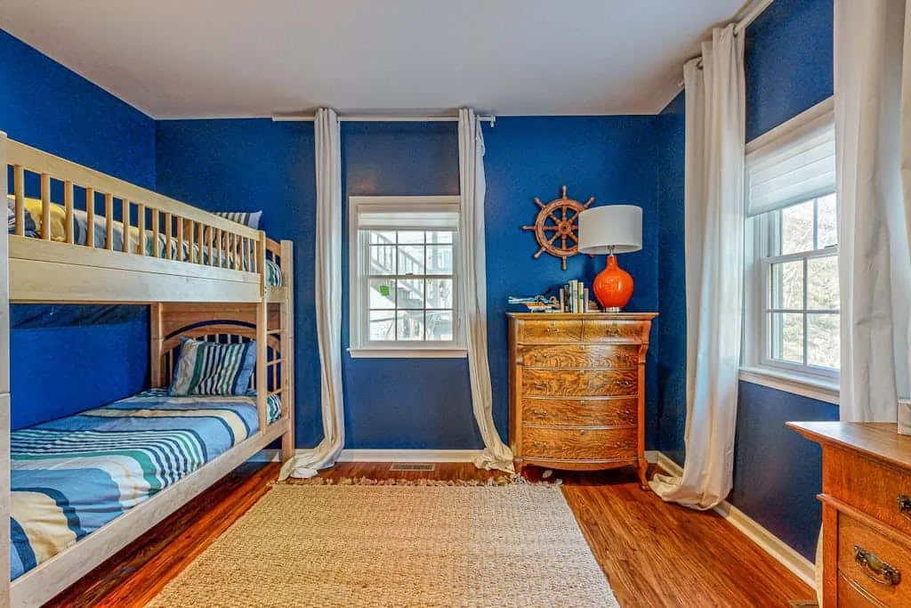A blue bedroom with bunk beds, a dresser, and windows.