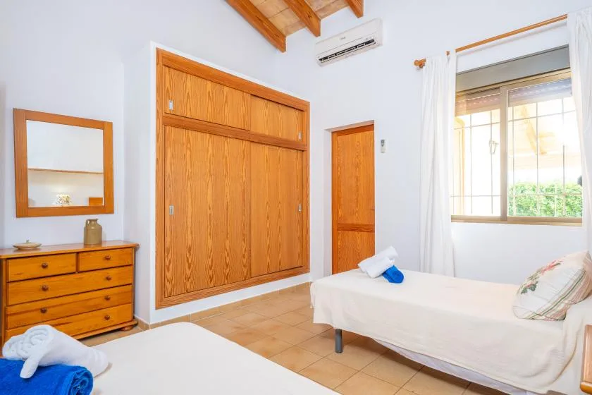 A bright bedroom with wooden closets, a bed, and a large window.