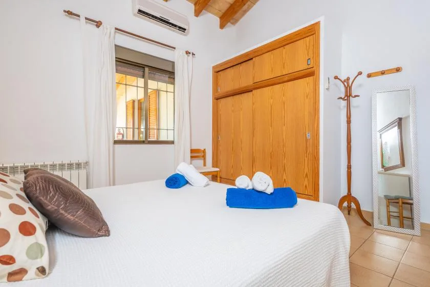 A bedroom with a white bed, blue towels, and a wooden wardrobe.