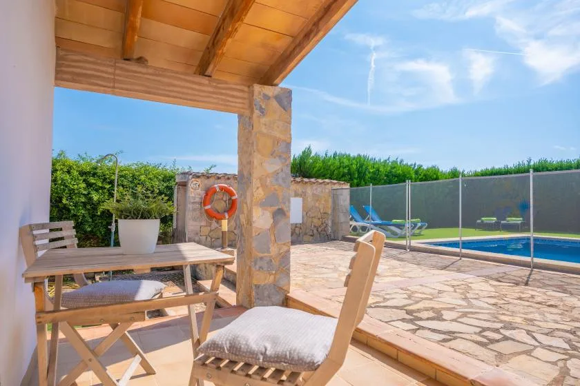 A covered patio with seating overlooks a paved outdoor area and swimming pool.