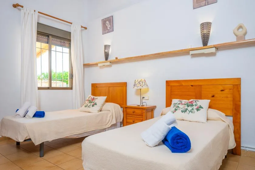 A bedroom with two beds, wooden headboards, and a window with curtains.