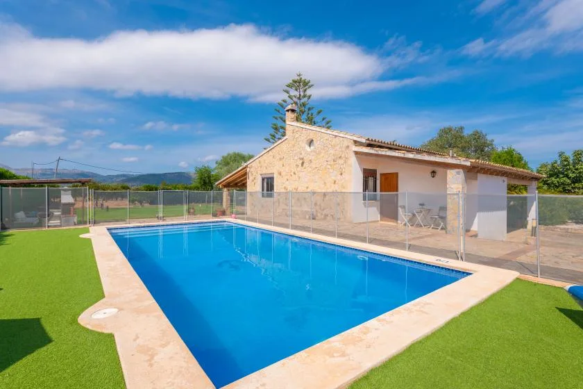 A swimming pool beside a stone-clad building, enclosed by a clear fence.