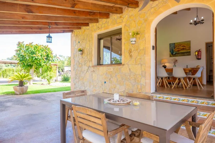 A covered patio with a dining table overlooks a garden and an indoor dining area.
