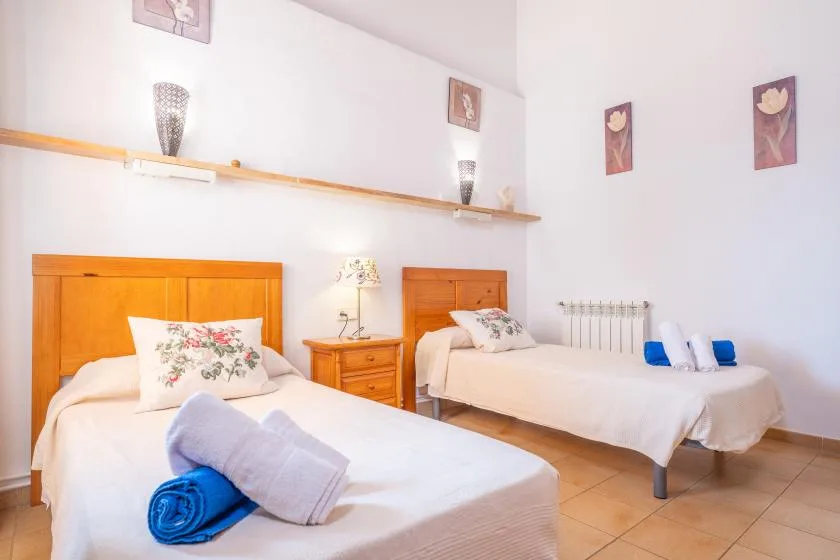 A bright bedroom with two beds, floral pillows, and folded towels.