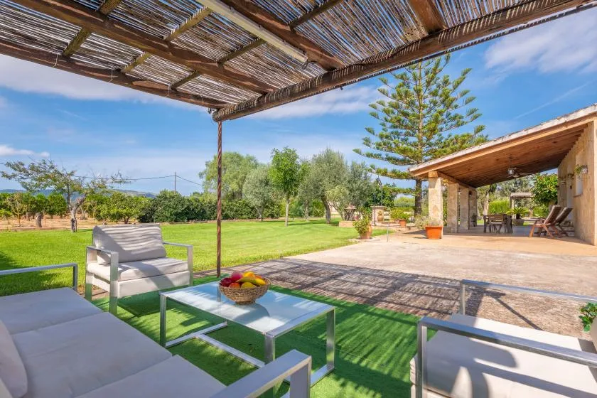 An outdoor patio with seating overlooks a green lawn beneath a shaded pergola.