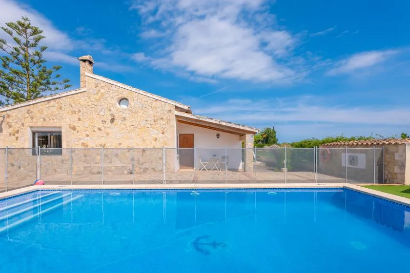 A swimming pool in front of a stone house, with a covered patio behind it.