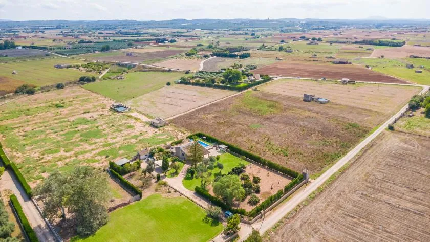 An aerial view shows open farmland divided into fields, with a landscaped property in the foreground.