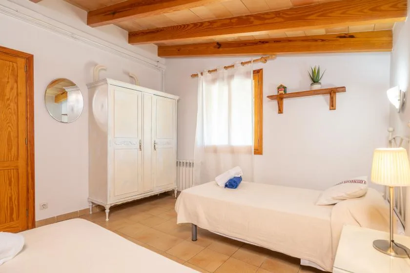 A bright bedroom with a bed, white wardrobe, and exposed wooden ceiling beams.
