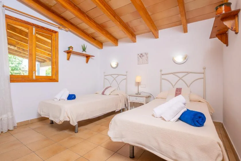 A bedroom with two beds, pale bedding, and exposed wooden ceiling beams.