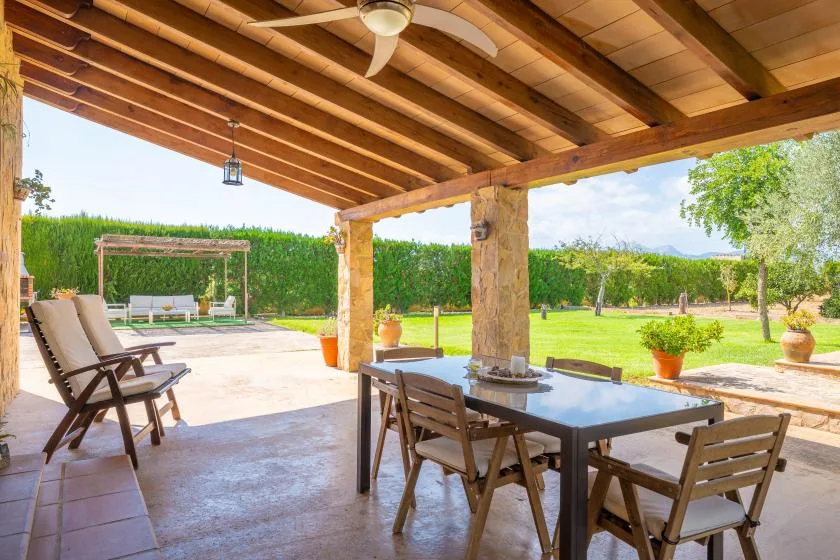 A covered patio has a dining table and seating overlooking a green garden.
