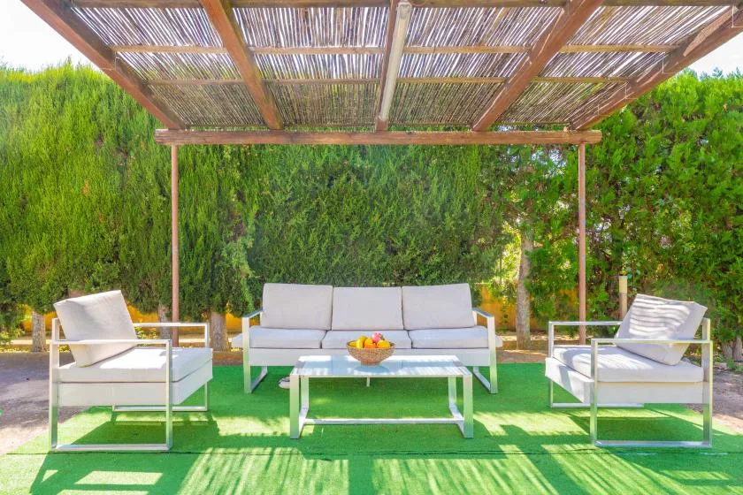 Outdoor seating beneath a wooden pergola, with a table and greenery.