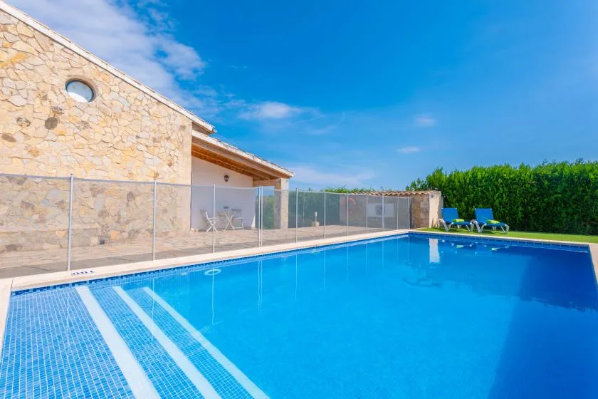 An outdoor swimming pool beside a stone building, with lounge chairs nearby.