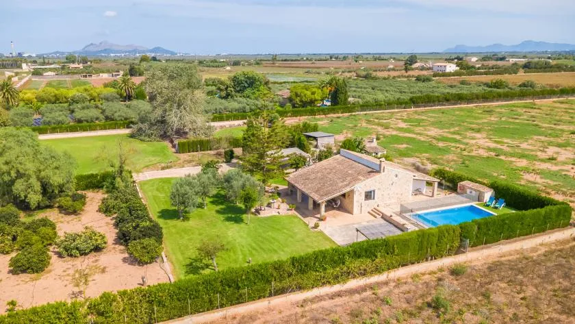 A countryside house with a swimming pool sits among green fields and gardens.