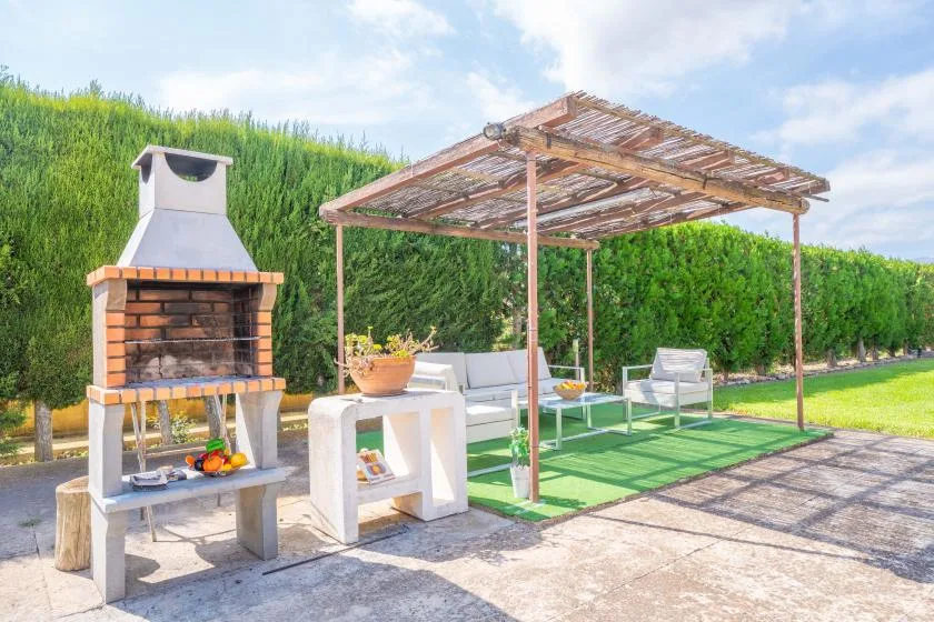 An outdoor patio has a brick barbecue beside shaded seating and a table.