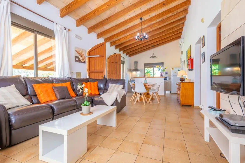 A bright living and dining area with seating, a dining table, and exposed wooden ceiling beams.
