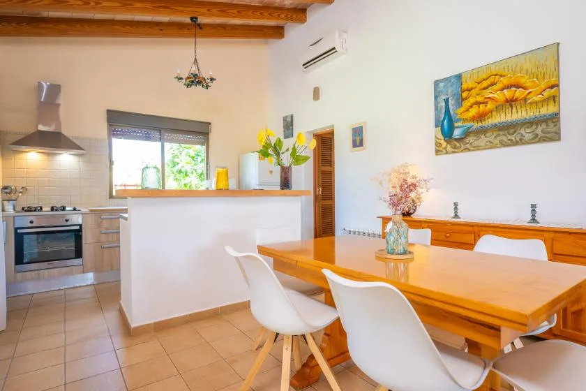 A dining area beside an open kitchen, with a wooden table and white seating.