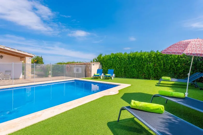 An outdoor swimming pool beside a lawn with reclining seats.