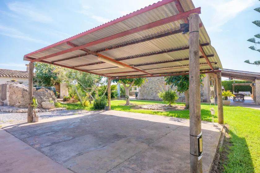 A covered outdoor patio with a paved floor and garden greenery.