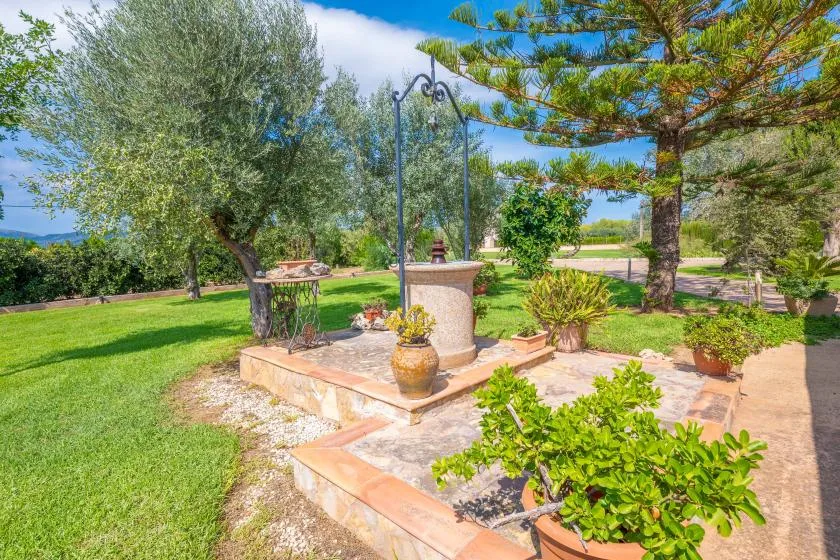 A landscaped garden with a stone fountain, potted plants, and a paved path.