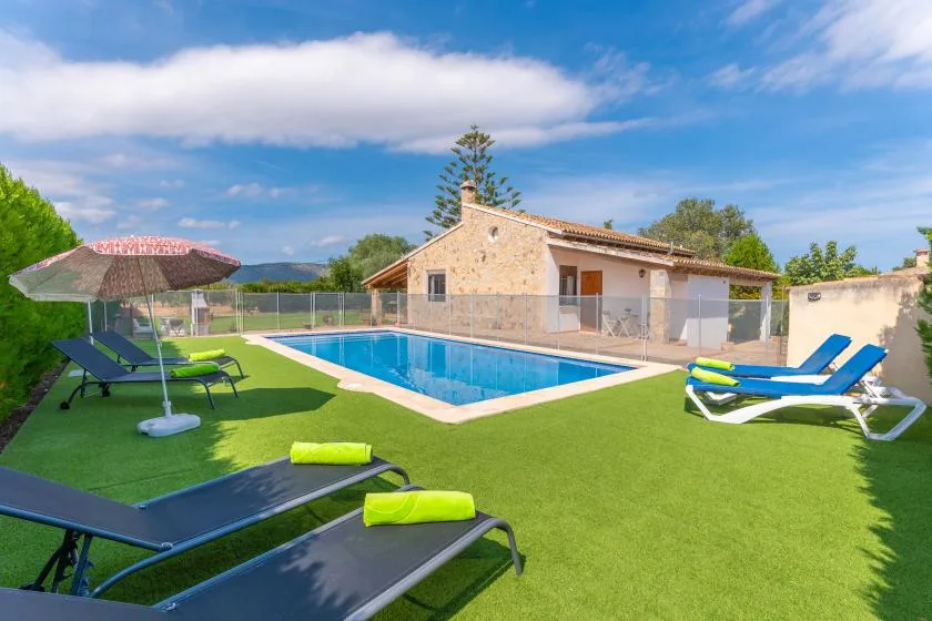 A swimming pool beside a stone house, with lounge chairs on the surrounding lawn.