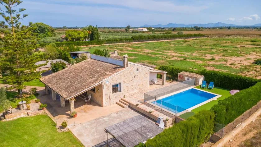 A stone house with a swimming pool sits beside open fields.