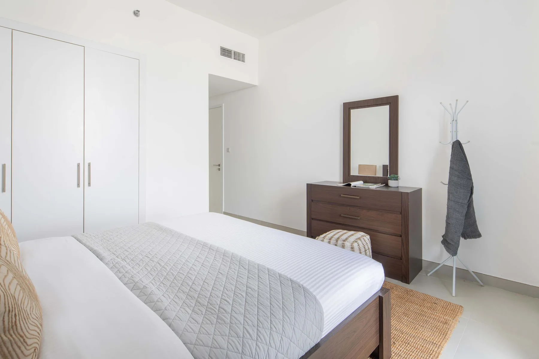 Un dormitorio luminoso con una cama, una cómoda y un perchero de pie.