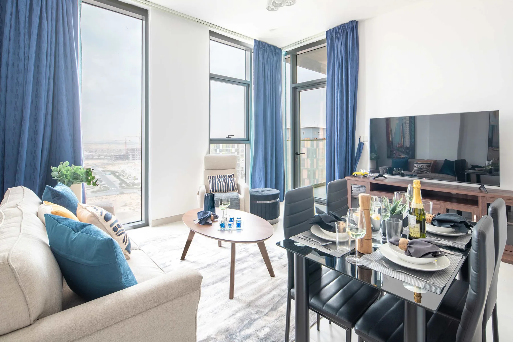 Una luminosa sala de estar y comedor tiene cortinas azules y un televisor grande.