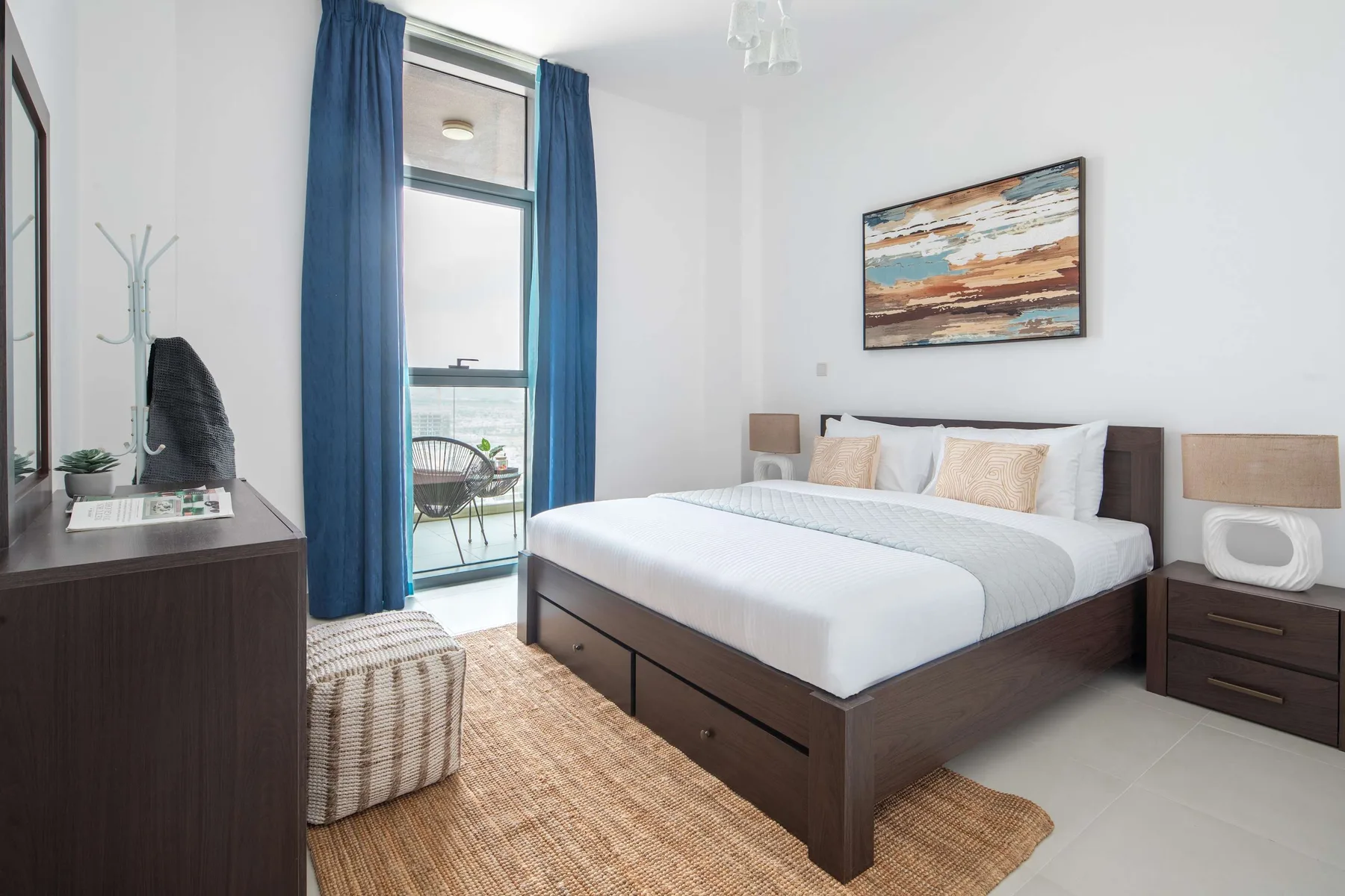 Un dormitorio luminoso con una cama, cortinas azules y una alfombra tejida.