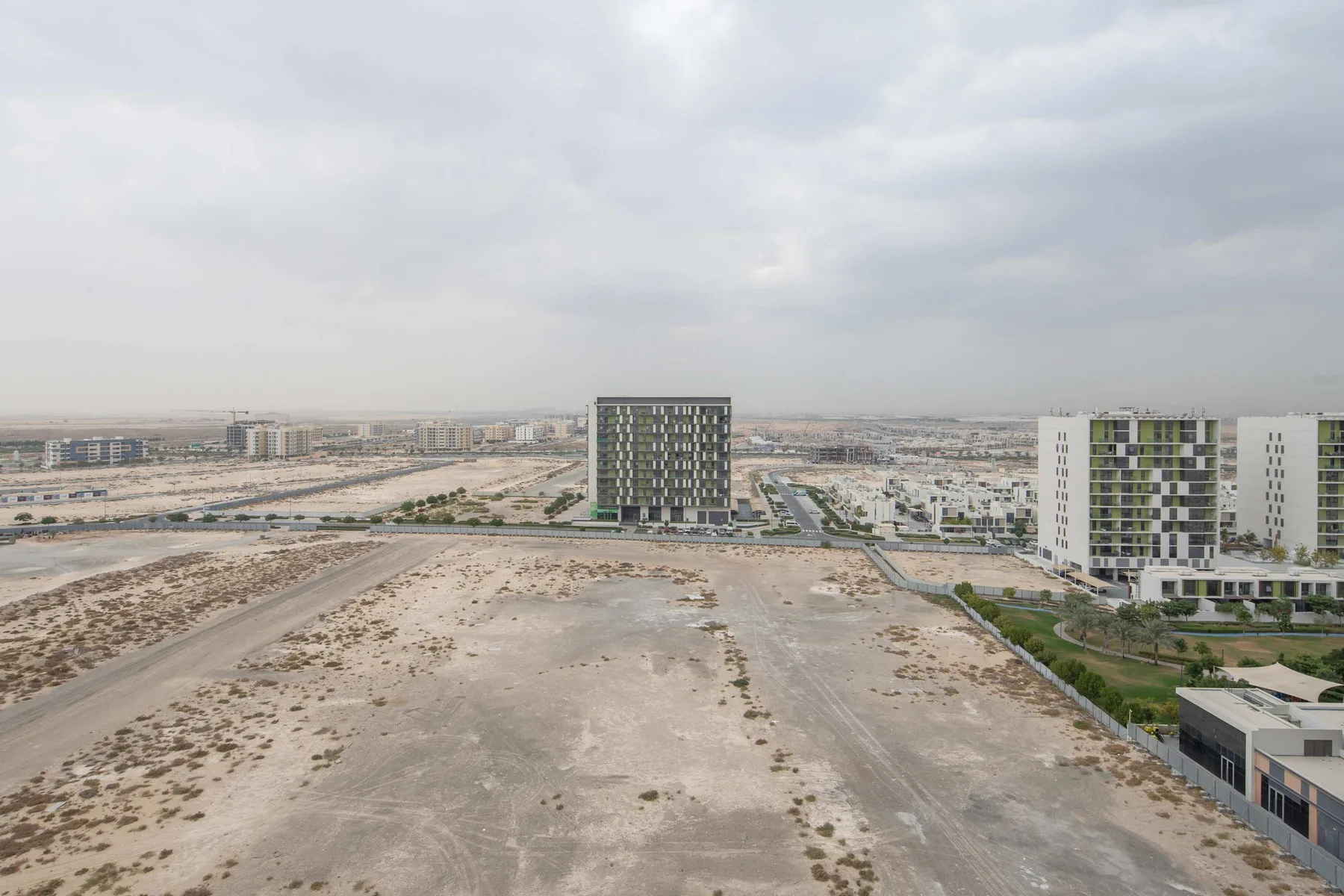 Vista aérea de edificios de apartamentos junto a un amplio terreno abierto bajo un cielo nublado.