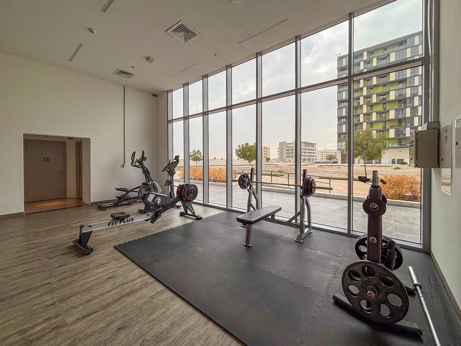 Un gimnasio con equipo de ejercicio junto a ventanas de piso a techo.