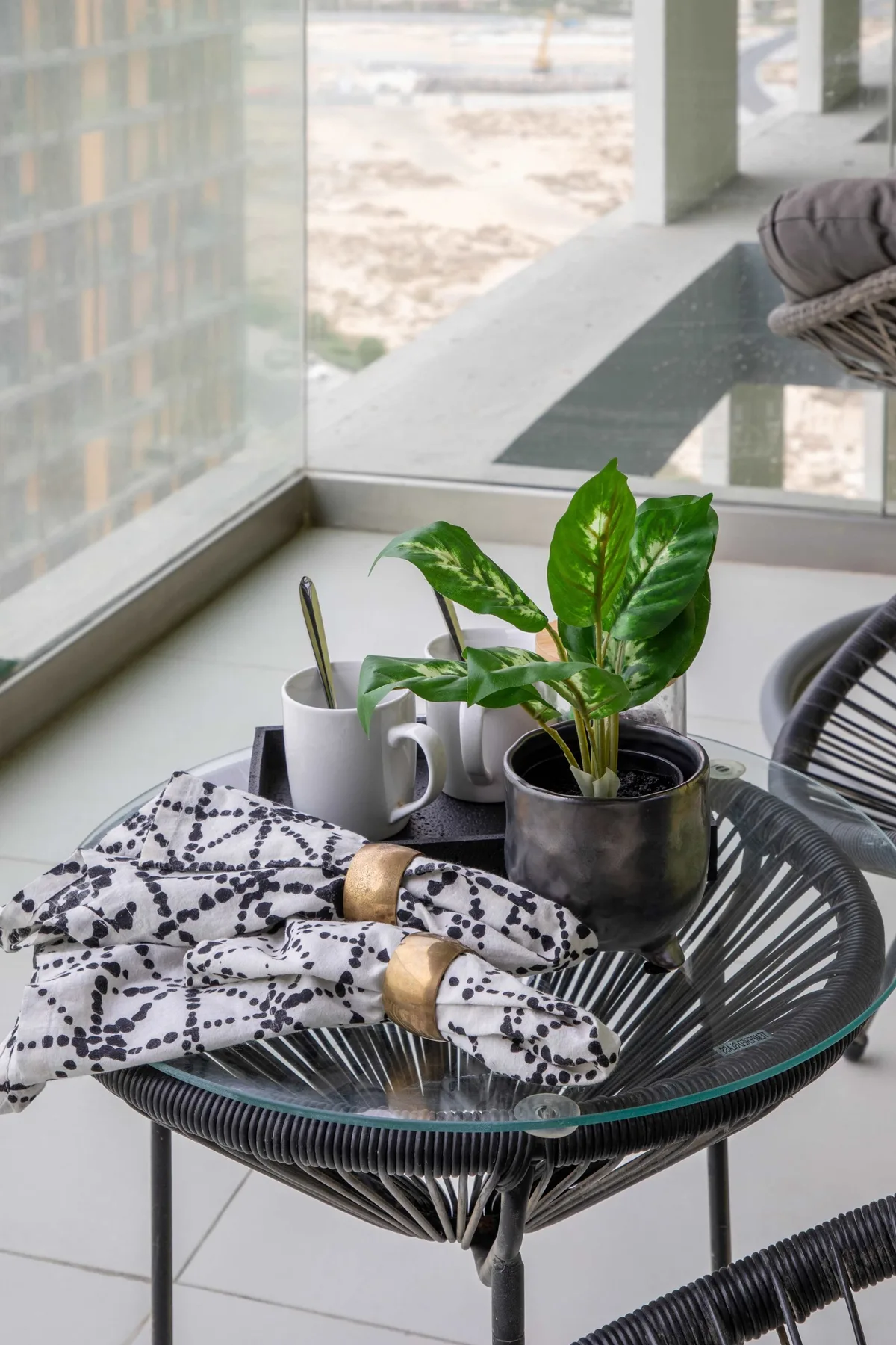 Una mesa de patio con tapa de vidrio tiene plantas en macetas y una tela estampada doblada.